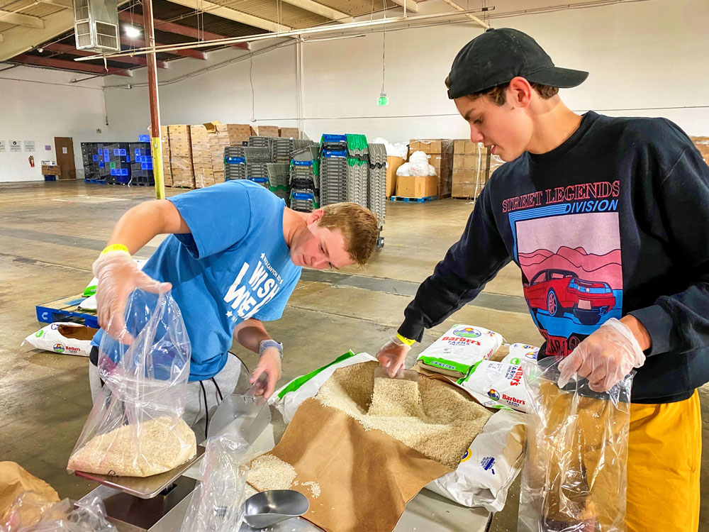 Photo of Sophomore Kian Olsen and junior William Musso, scoop and weigh rice.