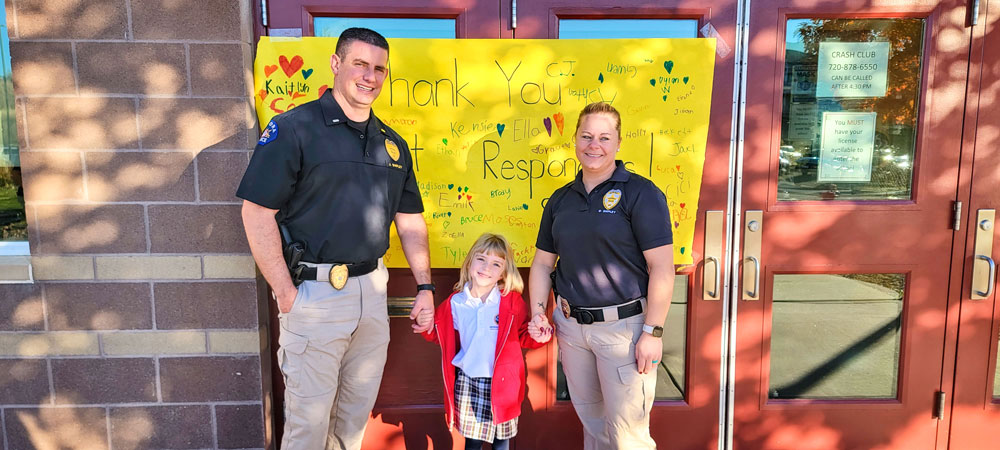 Photo of First grader Sadie Shipley stands proud in front of her classroom banner welcoming and thanking her parents – both Aurora Police Officers – and all first responders.