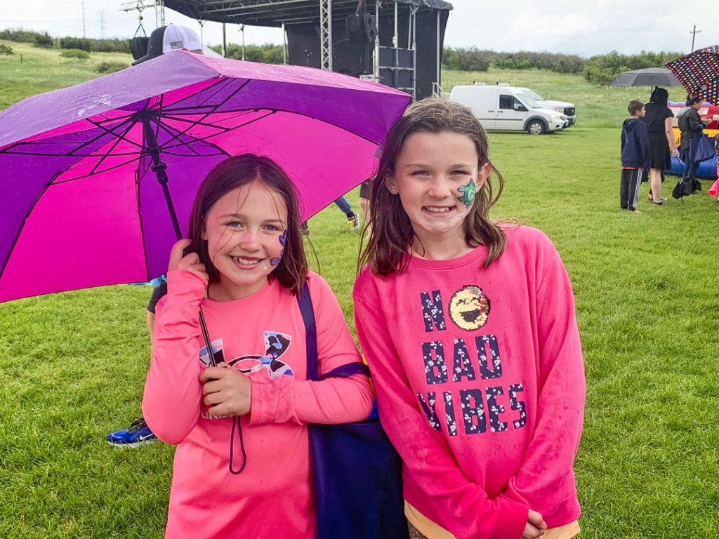girls in pink shirts at outdoor event with umbrella