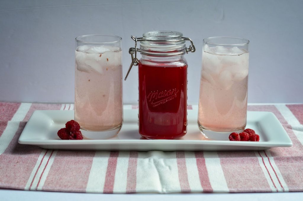 photo of two glasses of raspberry shrub and a mason jar