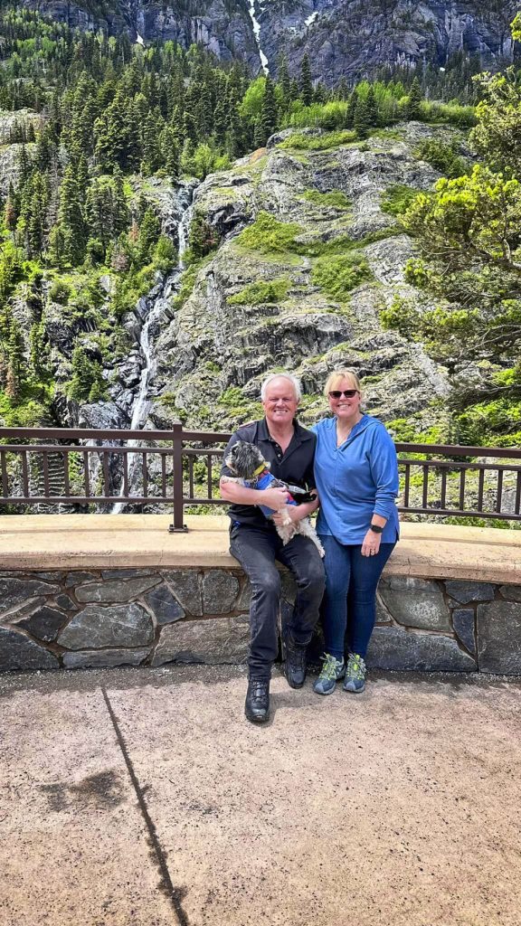 couple holding dog and in front of waterfall