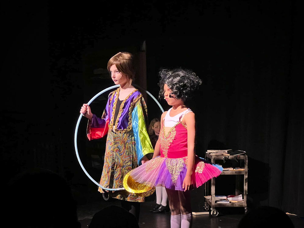 two girls stand on stage in colorful outfits