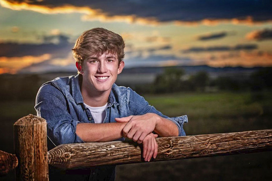 teen leaning on wood fence with sunset behind