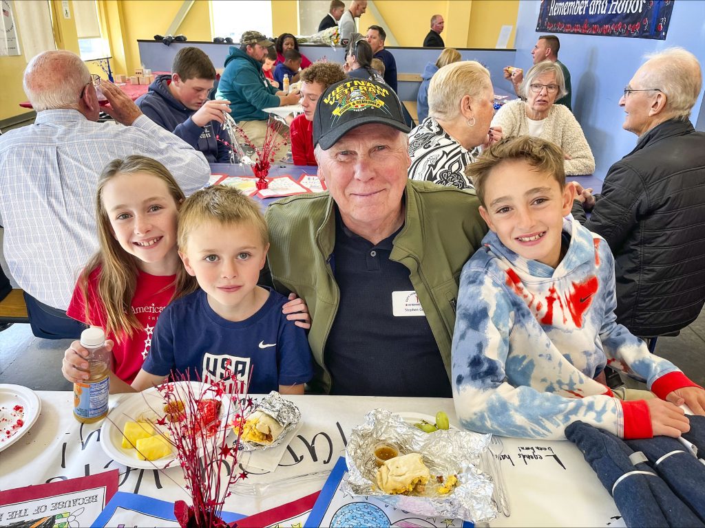 veteran and three kids sit at table with food