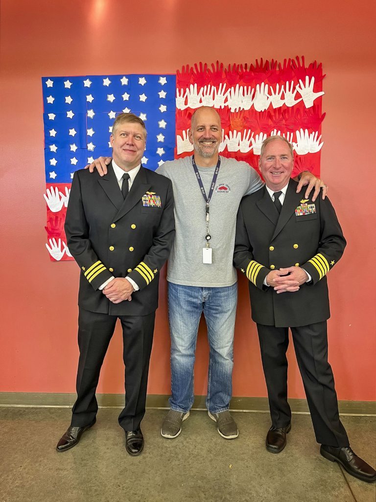 three men stand in front of flag made from kids