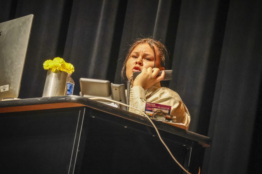 female student holding phone at desk on stage