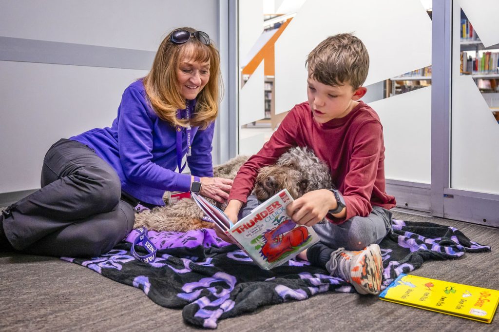 lady, boy and dog in room and boy is reading a book