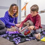 lady, boy and dog in room and boy is reading a book