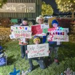 four kids stand outside holding paper