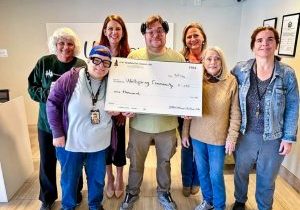 Mountain Pine Woman’s Club members Carol Bernard (back row, far left) and Karen Montgomery (second to right first row) share the joy of giving by providing $1,000 to Wellspring Community. Nicole DeVries, executive director of Wellspring (back row, right) receives the check.