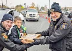DCSO Deputy Lee Jazombek (left) and CSV Frank Ruggieri (right) accept a box of donuts from a young citizen during a drug take-back event earlier this year.
