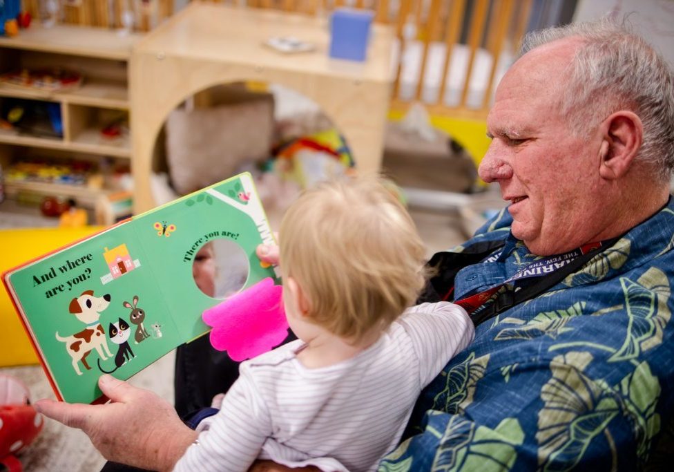 An Early Childhood Service Corps (ECSC) volunteer, Chuck Sonderquist, reads to a program site student. ECSC connects older adults (50+) with early childhood education. 