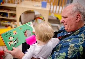 An Early Childhood Service Corps (ECSC) volunteer, Chuck Sonderquist, reads to a program site student. ECSC connects older adults (50+) with early childhood education. 